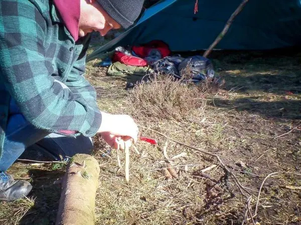 Messer bearbeitet Holzstücke zur Herstellung von Zunder neben einem Tarp