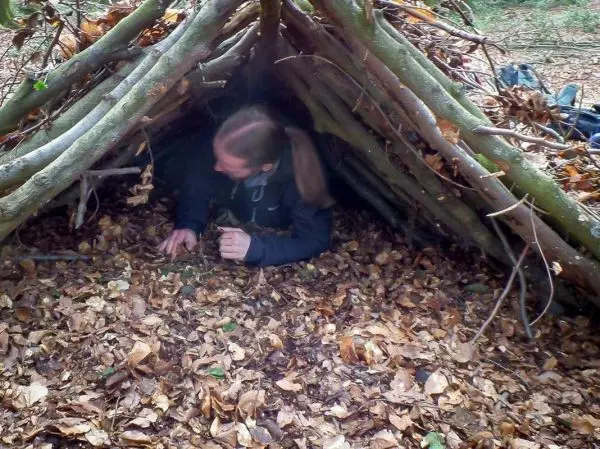 Person kriecht in eine selbstgebaute Laubhütte aus Ästen und Blättern