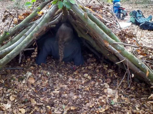 Person kriecht in eine selbstgebaute Laubhütte aus Ästen und Blättern