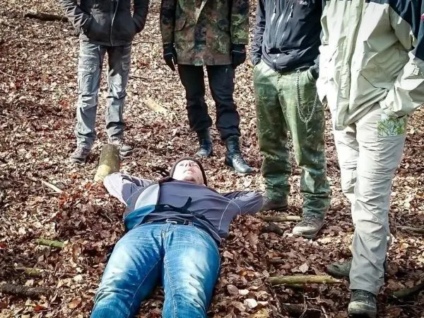 Person liegt auf dem Boden im Laub, umgeben von mehreren Personen