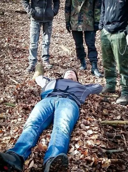 Person liegt auf dem Boden im Laub, umgeben von mehreren stehenden Personen