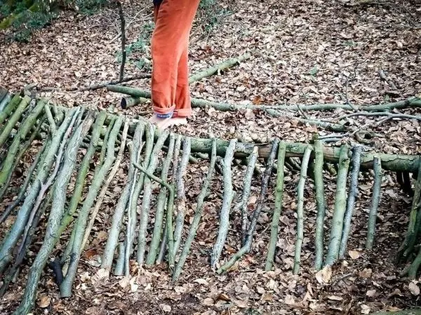 Person steht auf selbstgebauter Seilbrücke aus Ästen im Wald