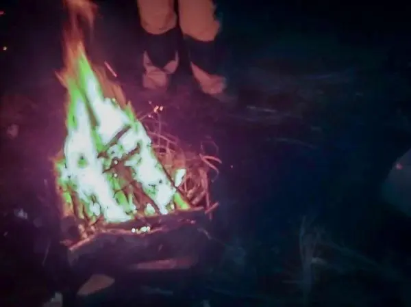 Person steht neben einem brennenden Feuer im Dunkeln