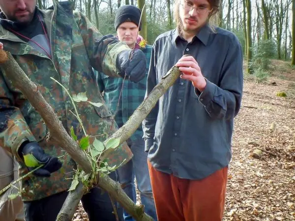 Person zeigt anderen Personen eine selbstgebaute Struktur aus Ästen