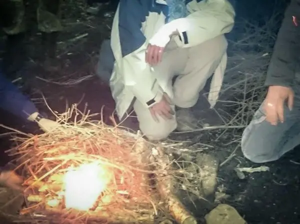Personen knien um ein Feuer aus Ästen und Holz