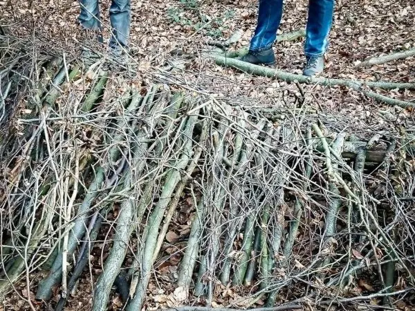 Selbstgebaute Holzstruktur aus Ästen im Wald, zwei Beine stehen daneben