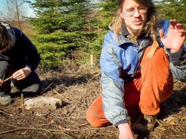 Zwei Personen arbeiten im Wald, eine kniet und bearbeitet Holz