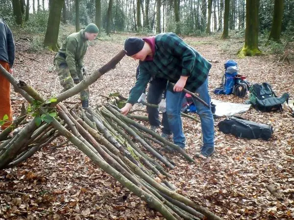 Zwei Personen bauen eine Holzstruktur aus Ästen im Wald