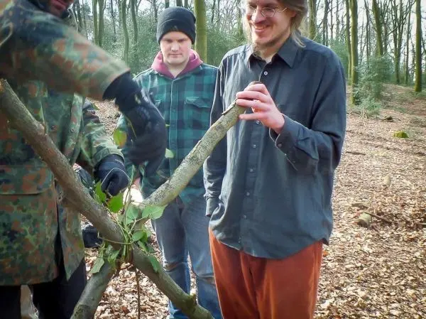 Zwei Personen beobachten, wie ein dritter Astwerk mit Blättern bindet