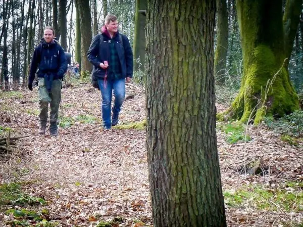 Zwei Personen gehen auf einem Waldweg zwischen Bäumen und Laub