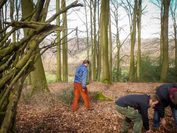 Zwei Personen sammeln Laub im Wald, im Hintergrund eine selbstgebaute Struktur