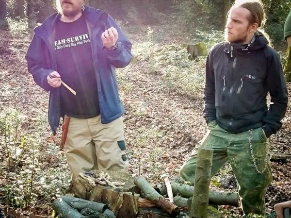 Zwei Personen stehen neben einem Holzstapel und diskutieren über Holzarbeiten