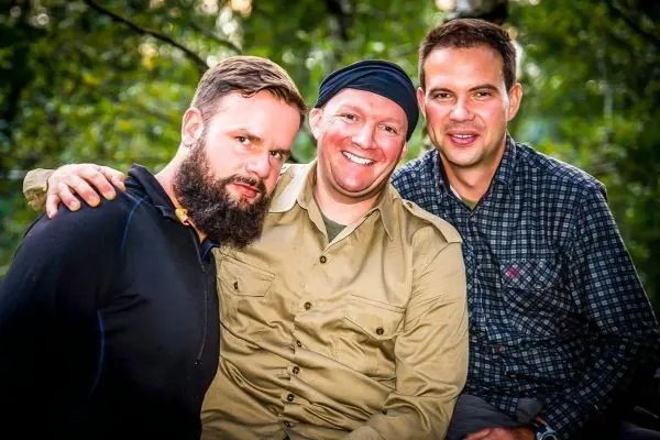 Drei Männer posieren lächelnd vor einer grünen Hintergrundlandschaft