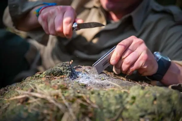 Feuerstahl erzeugt Funken auf Zunder mit einem Messer auf einem Stein