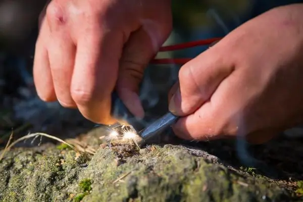 Hände erzeugen Funken mit Feuerstahl auf einem Stein
