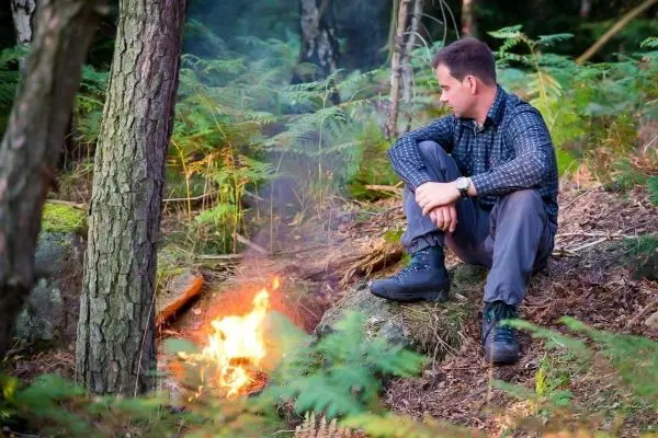 Kleine Flamme brennt neben sitzendem Mann im Wald