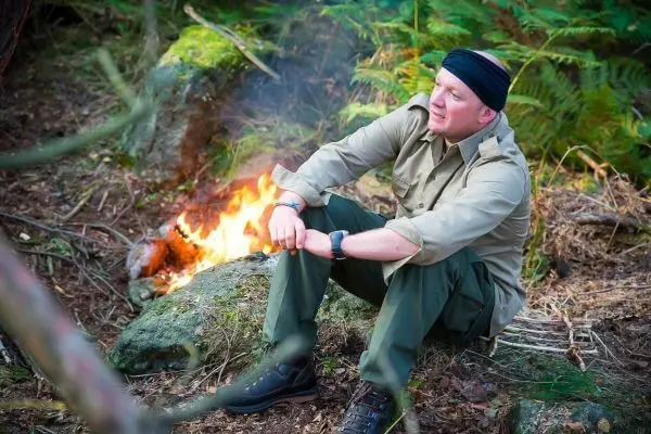 Kleine Flamme brennt neben sitzender Person auf einem Stein im Wald
