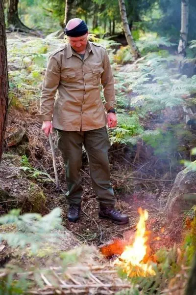 Kleine Flamme glimmt im Wald, Mann steht daneben mit Stock