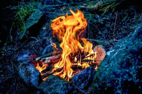 Kleine Flamme zwischen Steinen brennt auf Holzstücken