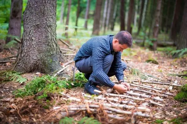 Mann arrangiert kleine Äste auf dem Waldboden für eine Konstruktion