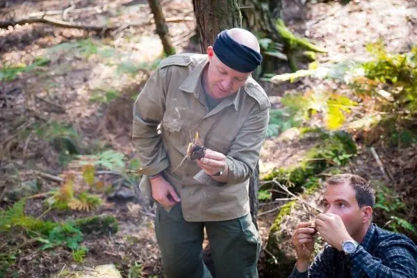 Mann hält brennendes Zundernest in der Hand, während ein anderer Mann daneben sitzt