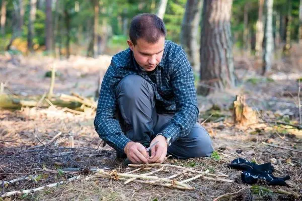 Mann kniet im Wald und bereitet Zunder aus Ästen vor