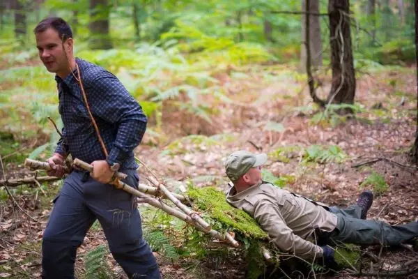 Mann zieht improvisierte Trage mit einem anderen Mann durch den Wald