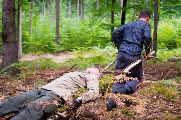 Mann zieht improvisierte Trage mit einem anderen Mann durch den Wald