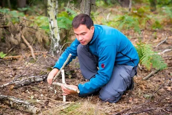 Person baut eine Konstruktion aus Ästen im Wald
