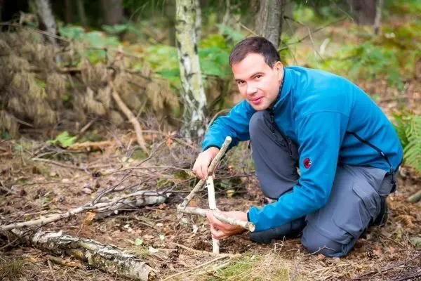 Person baut eine Struktur aus Ästen im Wald