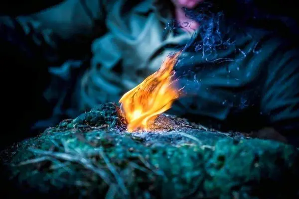 Person entzündet Feuer auf einem Untergrund aus Erde und Gras