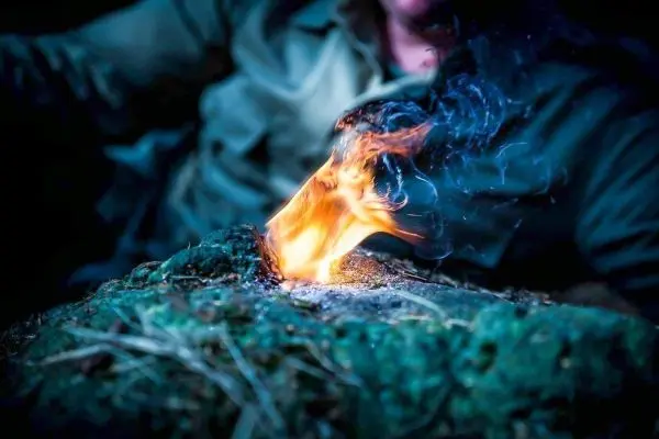 Person entzündet Feuer auf einem Untergrund aus Moos