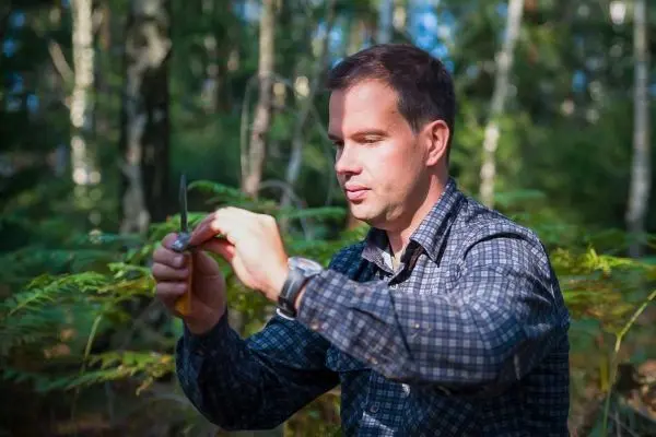 Person hält ein Messer und betrachtet es aufmerksam im Wald