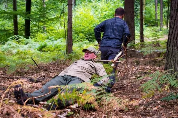 Person zieht liegende Person über den Boden im Wald