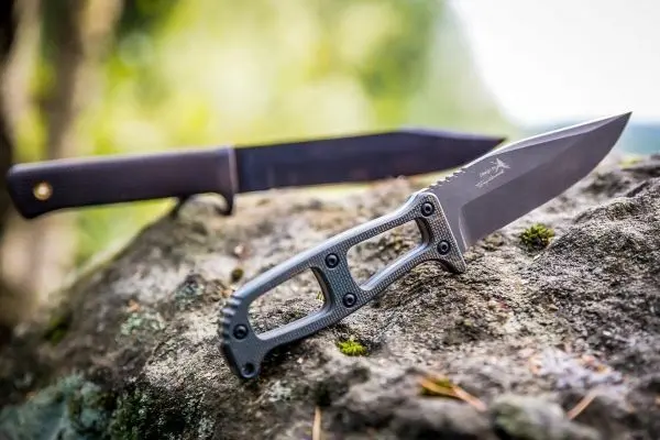 Zwei Messer liegen auf einem großen Stein, eines mit schwarzer Klinge und Griff