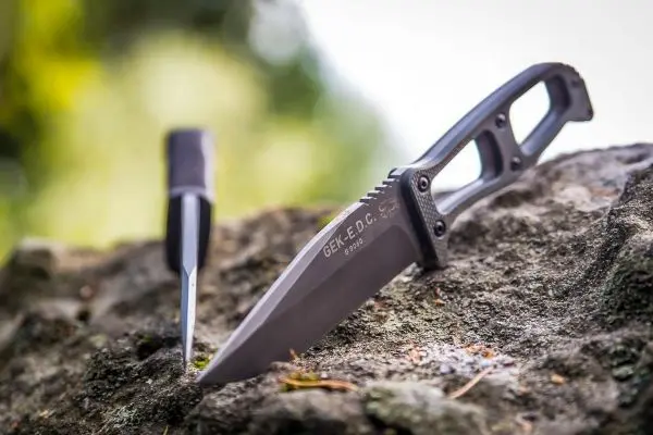 Zwei Messer liegen auf einem Stein, eines mit schwarzer Klinge und Griff