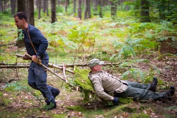Zwei Personen transportieren eine improvisierte Trage durch den Wald