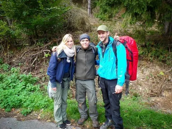 Drei Personen mit Rucksäcken stehen vor einer bewaldeten Kulisse