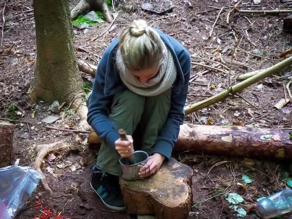 Eine Person bearbeitet einen Metallbecher mit einem Stock auf einem Holzstück