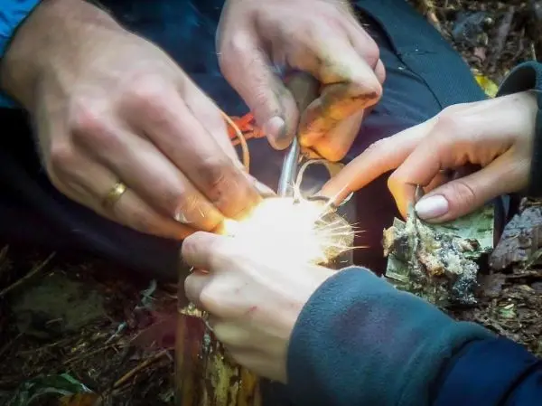 Feuerstahl erzeugt Funken auf Zunder zwischen zwei Händen