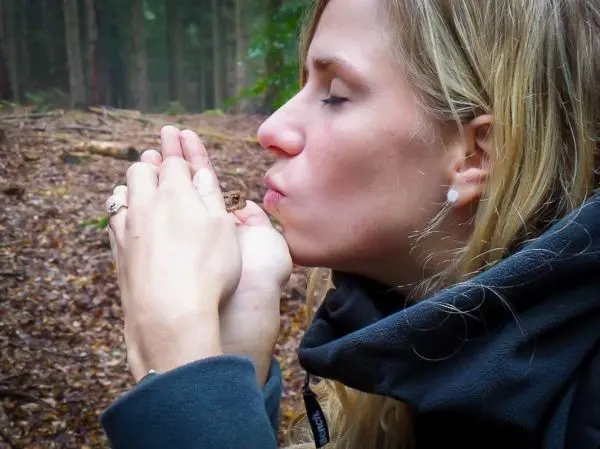Frau bläst in die Hände, während sie einen kleinen Gegenstand hält