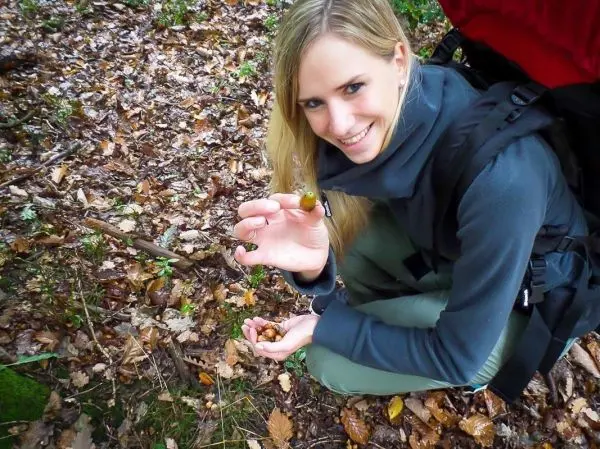 Frau hält eine kleine Frucht in der Hand, sitzt auf dem Waldboden