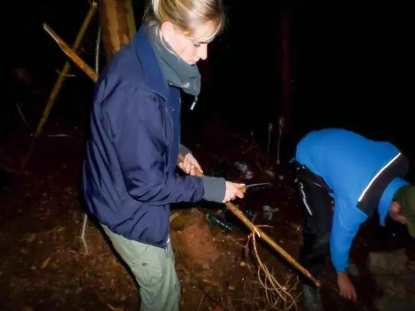 Frau schneidet mit einem Messer einen Stock im Wald