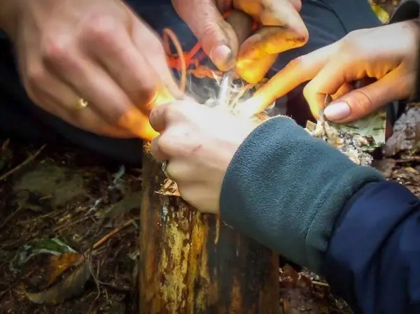 Hände entzünden Feuer mit Zunder auf einem Baumstamm beim Survival Training