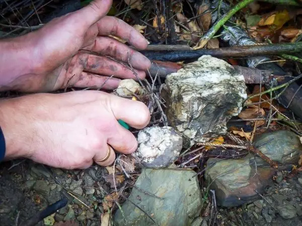Hände halten einen Stein und bearbeiten ihn mit einem Messer auf dem Boden