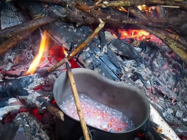 Kessel erhitzt Wasser über einem kleinen Bodenfeuer mit Glut und Flamme