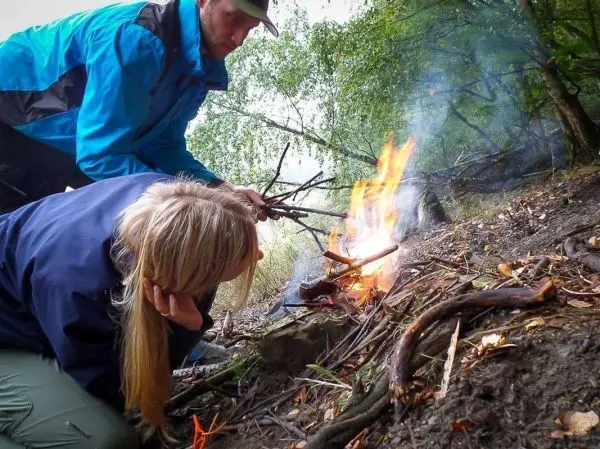 Kleine Flamme brennt zwischen Ästen, während eine Person Zunder hinzufügt