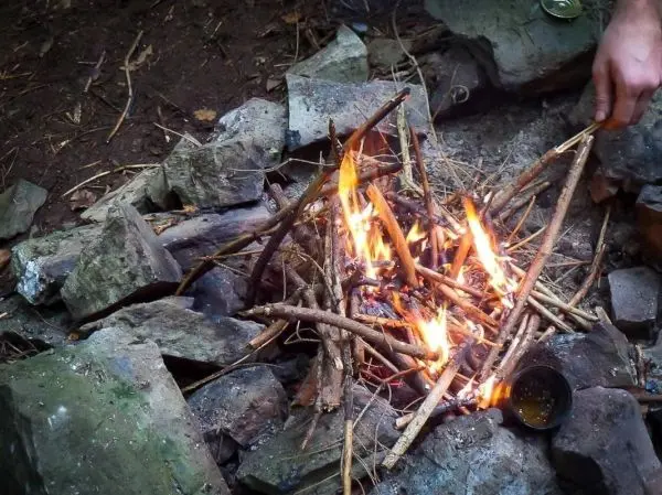 Kleine Flamme brennt zwischen Holzstücken in einer Steinkonstruktion