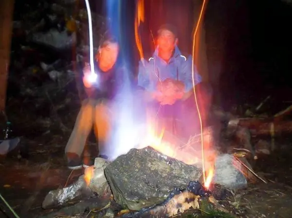 Kleine Flamme brennt zwischen Steinen, zwei Personen sitzen daneben