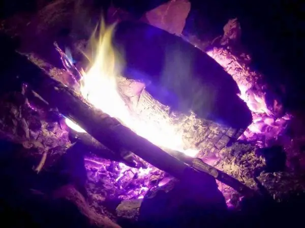 Kleine Flamme leuchtet zwischen glühenden Holzstücken im Feuer